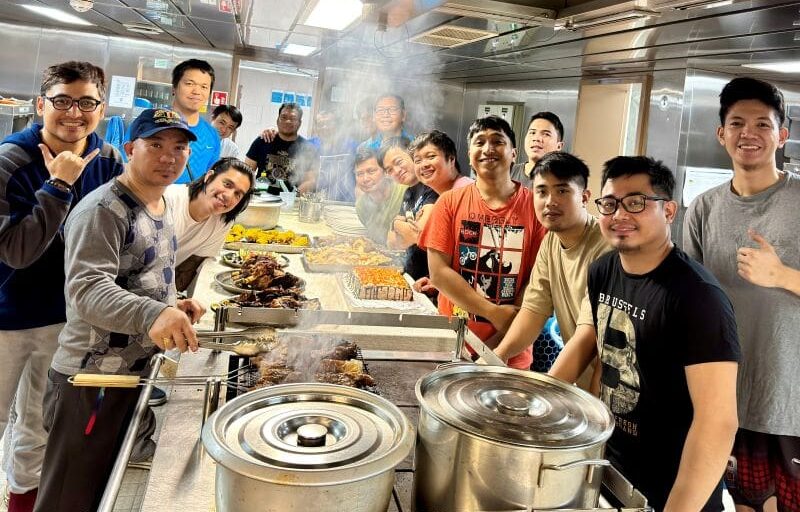Vessel crew posing together in the galley around a big feast of food.