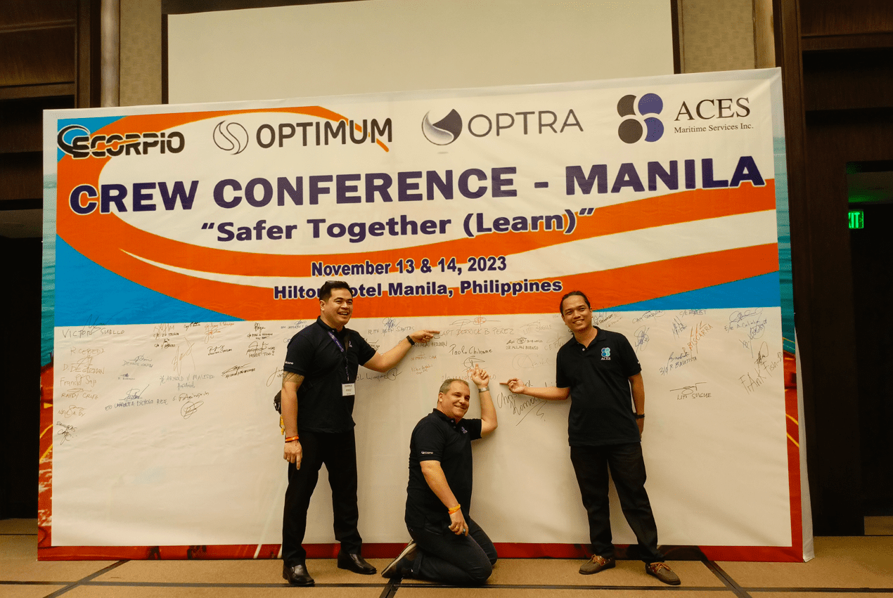 Three men standing in front of a sign, pointing to their names signed on it.