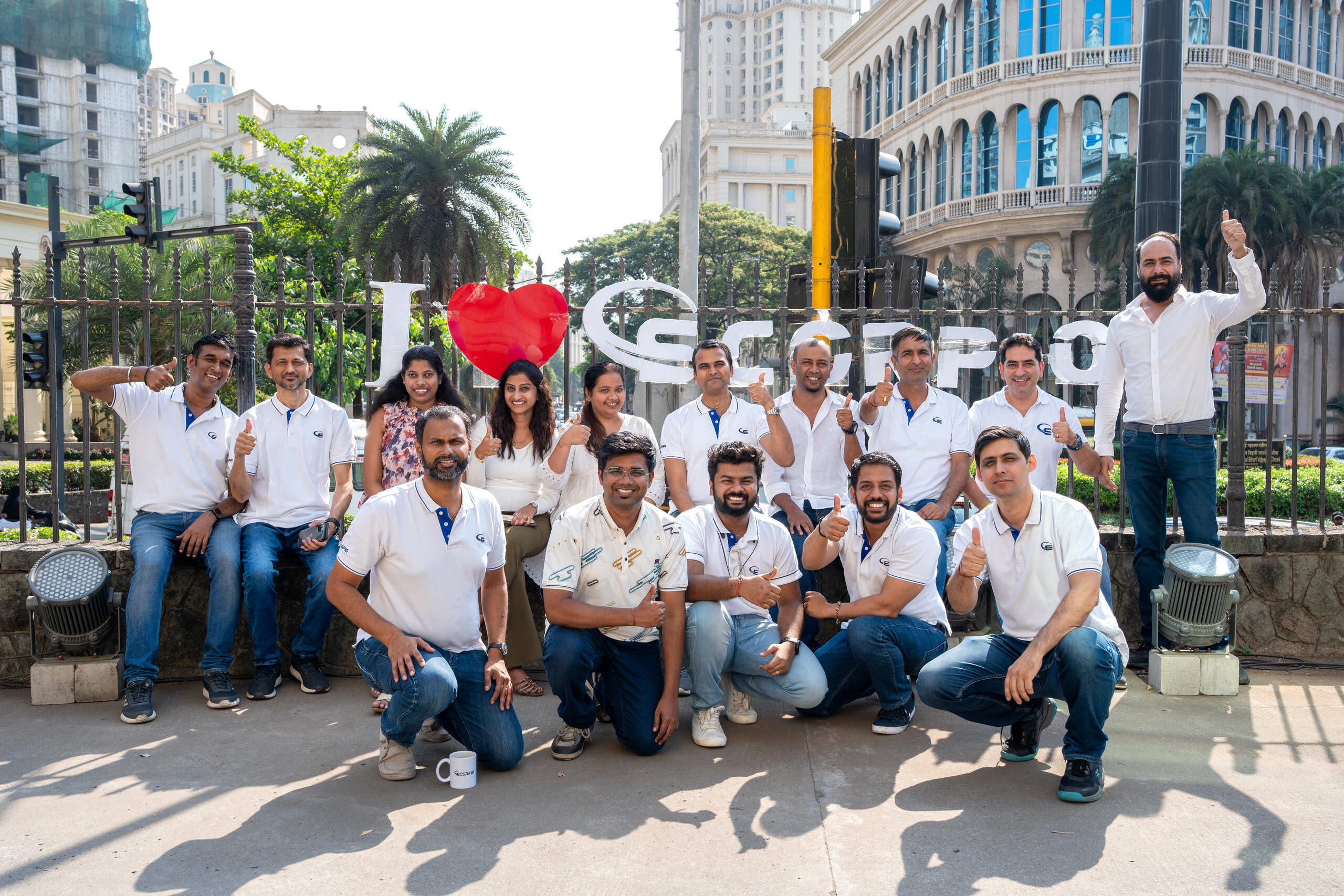 Group photo with thumbs up in front of park with 'I love Scorpio' sign.