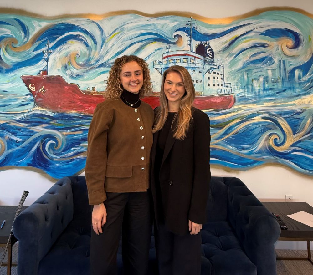 Two women standing in front of a wall mural of a ship.