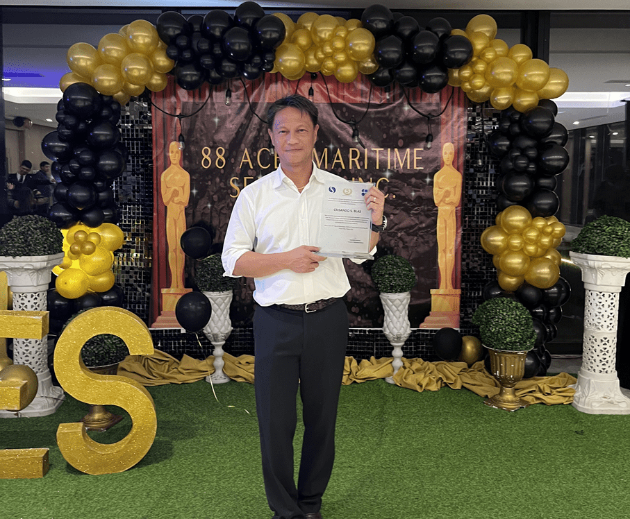 Man holding an award certificate with balloons in the background.