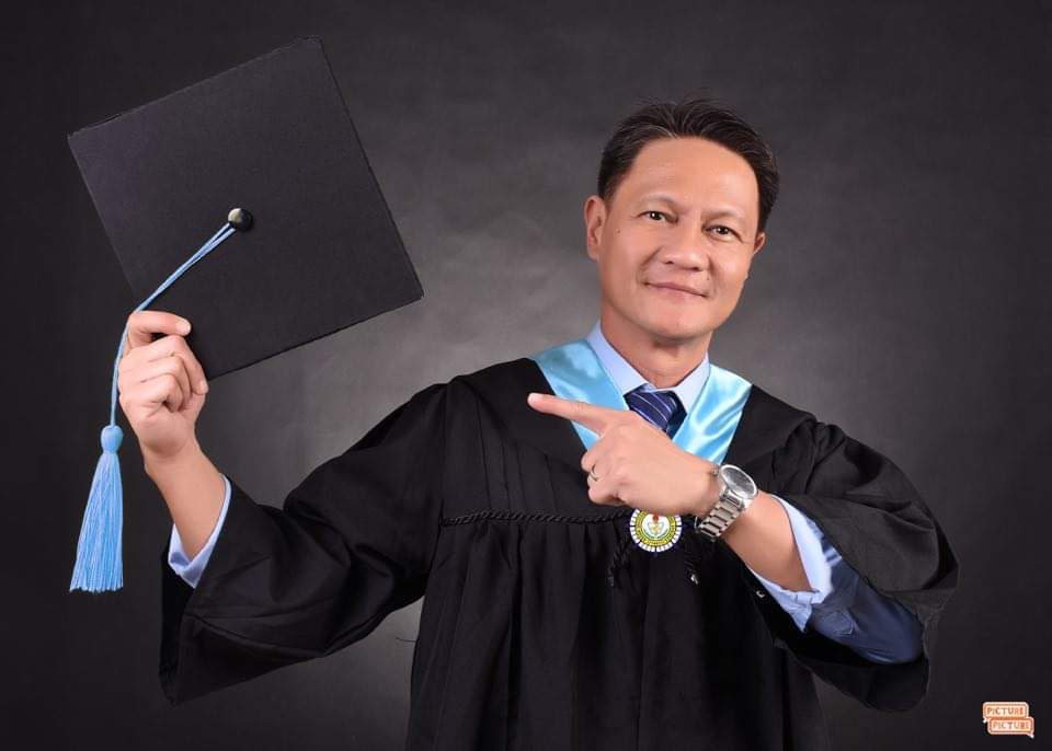 Man in graduation costume holding his cap to the side 