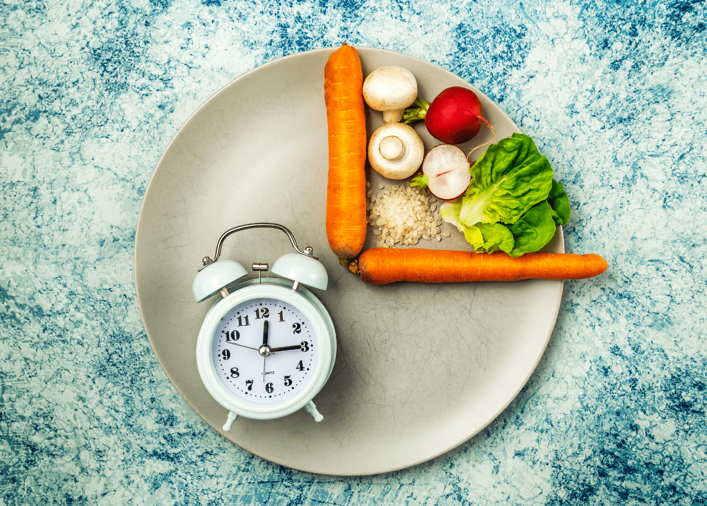 Plate with carrots, vegetables, and rice arranged in a small portion beside an analog alarm clock, symbolizing timed eating or dieting.