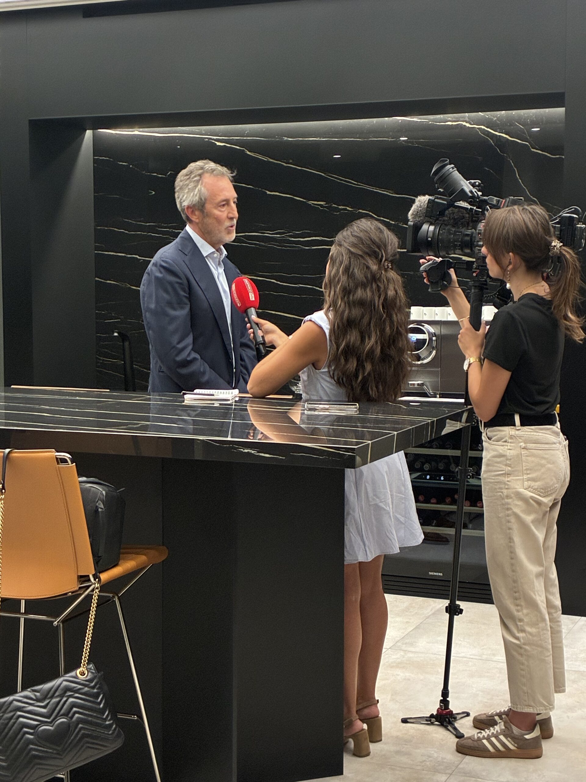 two women interviewing a man with a red microphone and a video camera.